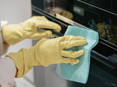 woman wearing pink rubber gloves wiping the oven handle with a cloth