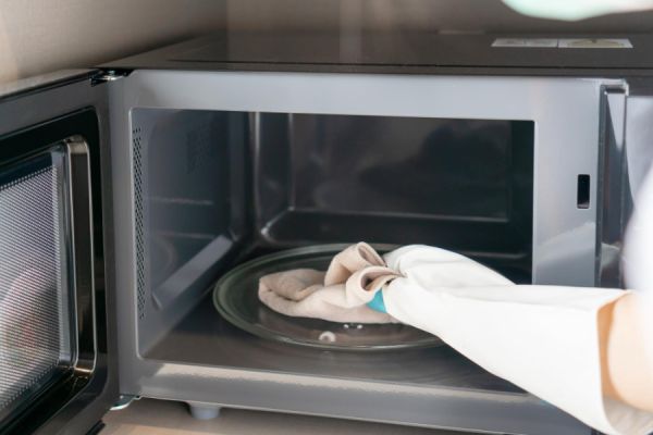 hand in a pink rubber glove wiping the inside of a microwave with a cloth