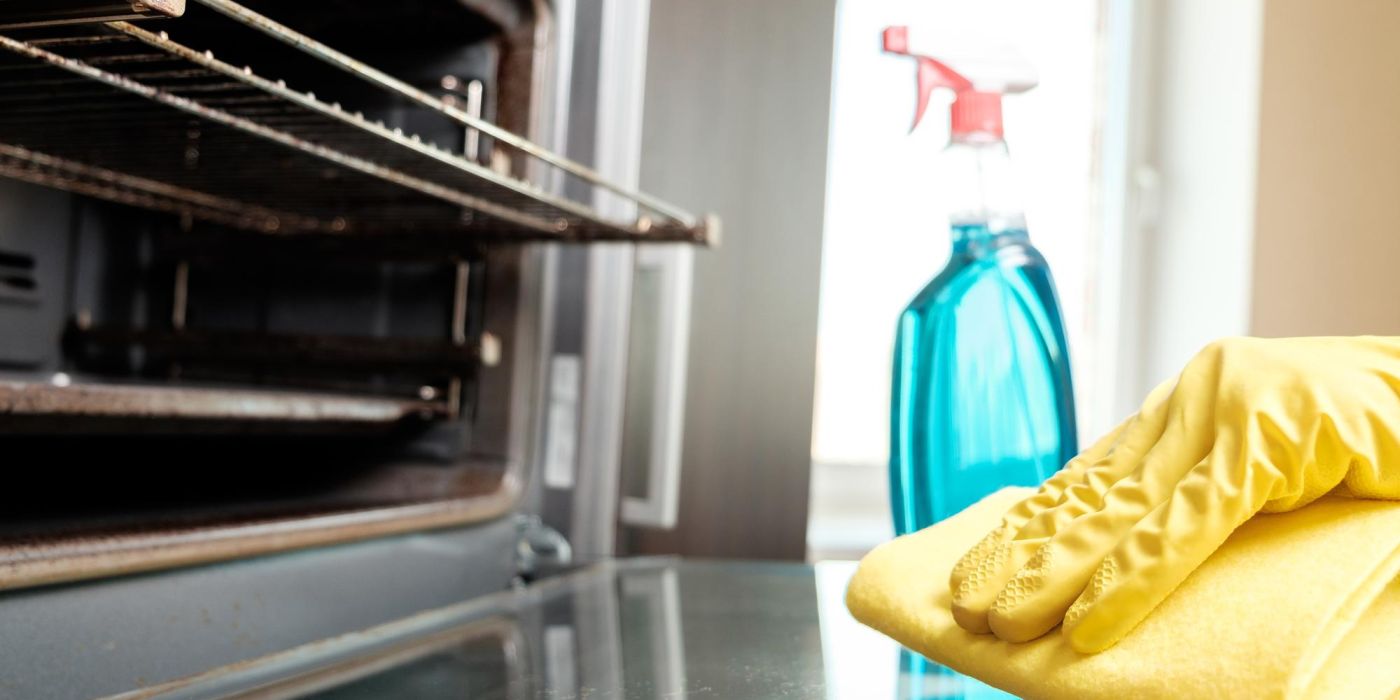 person wearing yellow rubber gloves with a yellow spong cloth wiping an oven door