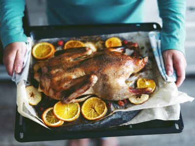 Woman cooking duck with vegetables and putting it into the oven.