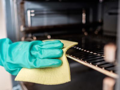 hand in grey rubber gloves wiping the oven shelf with a yellow sponge cloth