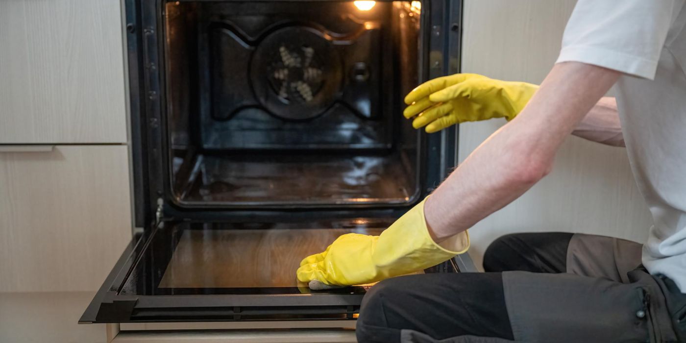 Person cleaning oven door glass with sponge with yellow rubber gloves