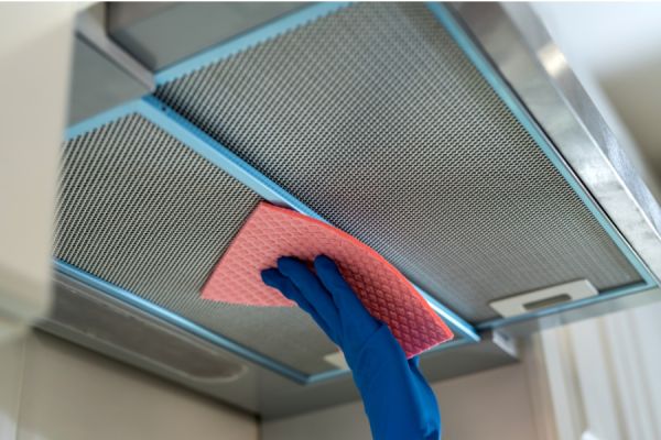 hand in a blue rubber glove wiping the mesh grill of a extractor hood with a sponge
